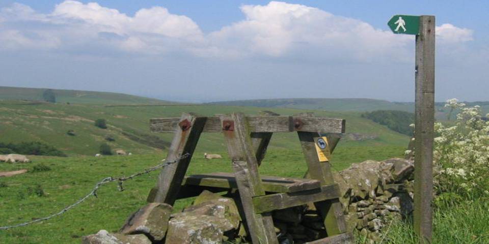 Countryside image of rolling hills with a walking access sign across a stone wall